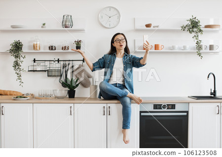Woman sitting on kitchen and having video call on smartphone Woman sitting on kitchen and having video call on smartphone 106123508