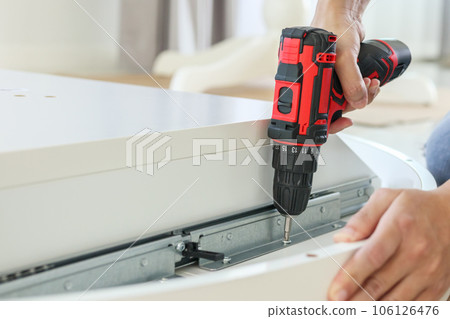 man assembling white table furniture at home using cordless screwdriver man assembling white table furniture at home using cordless screwdriver 106126476