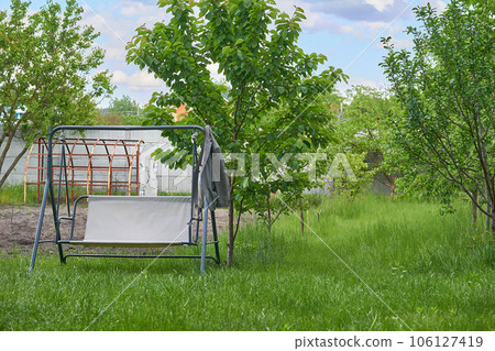 Garden metal swing for relaxing,resting on a summer spring plot on green grass Garden metal swing for relaxing,resting on a summer spring plot on green grass 106127419