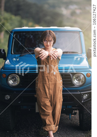 A woman posing with her hands out in front of a blue car 106127427