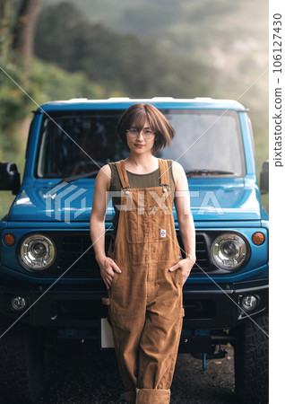 女人雙手插在口袋裡，在一輛藍色汽車前擺姿勢 106127430