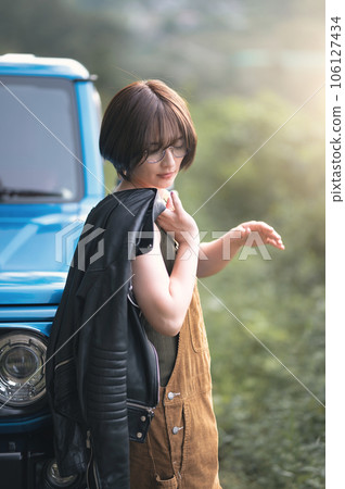 一個女人靠在一輛藍色的汽車上，看著自己的腳 106127434