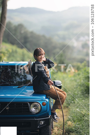 Sitting on the hood of a blue car, holding a stick and smiling Sitting on the hood of a blue car, holding a stick and smiling 106128788