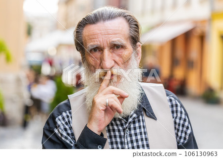 Senior man presses finger to lips makes silence hush sign do not tells gossip secret quiet in city 106130963