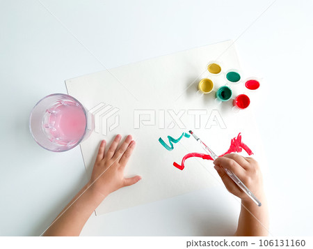 small child draws with paints and brush on white table. 106131160