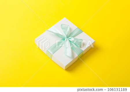 wrapped Christmas or other holiday handmade present in white paper with green ribbon on colored background. Present box, decoration of gift on colored table, top view with copy space 106131189
