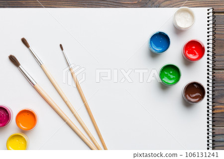 Album pages and paints, pencils, brush on a colored background. Top view with empty space. workplace for creativity. home teaching concept drawing 106131241