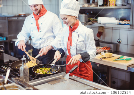 Chef woman and man cooking together in a restaurant kitchen Chef woman and man cooking together in a restaurant kitchen 106132534