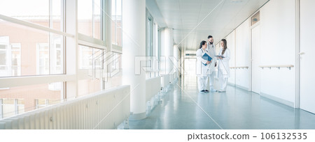 Three doctors on hospital corridor having short meeting 106132535