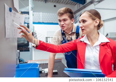 Worker and manager on factory floor discussing product specifications 106132541