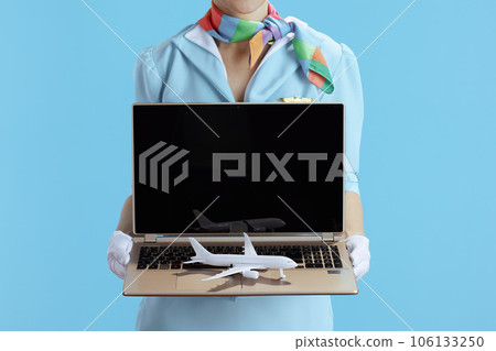 Stylish female stewardess on blue showing laptop blank screen Stylish female stewardess on blue showing laptop blank screen 106133250