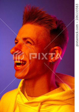 Wind blowing on face. Young guy in white hoodie posing against gradient purple background in neon light Wind blowing on face. Young guy in white hoodie posing against gradient purple background in neon light 106133563