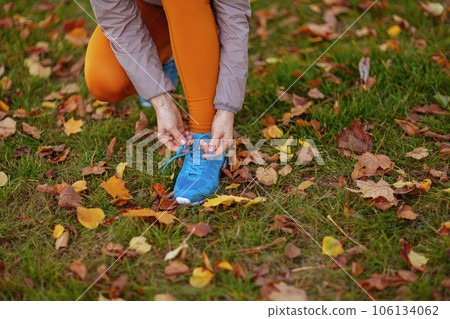 Elegant woman in fitness clothes in park tying shoelaces 106134062