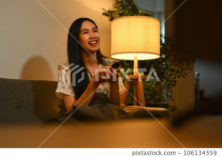 Nice, happy young woman watching tv on sofa, enjoying her leisure free time at home 106134359