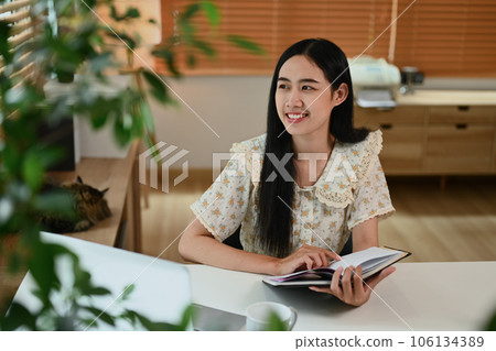 Positive young woman holding book and looking away, daydreaming and thinking on new ideas 106134389