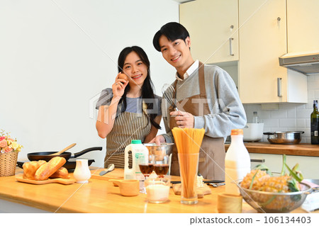 Beautiful young couple standing at worktop in the kitchen preparing and preparing breakfast together. 106134403