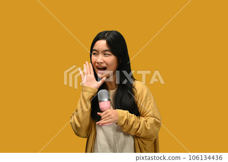 Teenage girl holding microphone singing karaoke, recording songs for contest isolated on yellow background 106134436