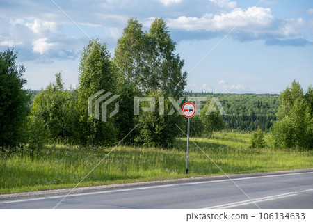 A road sign Overtaking is prohibited on a suburban highway through the forest on a sunny summer day. Beautiful landscape of nature and road. A road sign Overtaking is prohibited on a suburban highway through the forest on a sunny summer day. Beautiful landscape of nature and road. 106134633