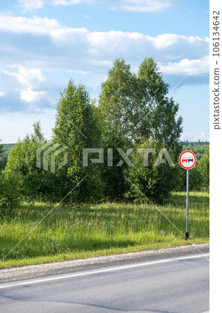 A road sign Overtaking is prohibited on a suburban highway through the forest on a sunny summer day. Beautiful landscape of nature and road. A road sign Overtaking is prohibited on a suburban highway through the forest on a sunny summer day. Beautiful landscape of nature and road. 106134642
