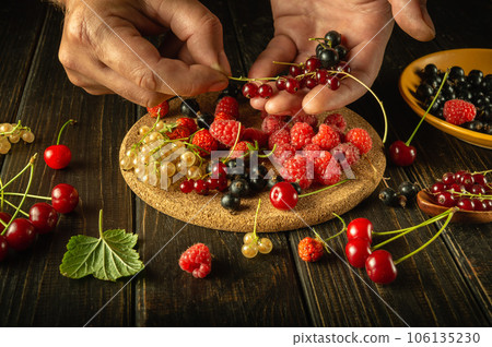 The chef selects berries with his hands to prepare a fruit drink or vitamin compote. The concept of vegetarian food from currants, raspberries and cherries The chef selects berries with his hands to prepare a fruit drink or vitamin compote. The concept of vegetarian food from currants, raspberries and cherries 106135230