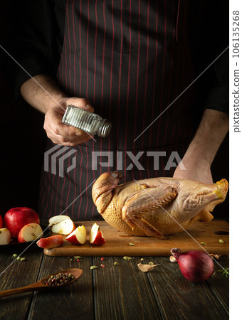 Cooking duck for lunch by the chef's hands. Raw duck with apples and spices on the kitchen table. The cook adds salt Cooking duck for lunch by the chef's hands. Raw duck with apples and spices on the kitchen table. The cook adds salt 106135268