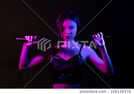 Beautiful young Asian woman holding katana sword by the point of knife in neon light. Beautiful young Asian woman holding katana sword by the point of knife in neon light. 106136370