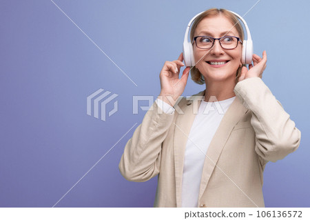close-up of 50s middle aged woman in jacket enjoying music with headphones on studio background with 106136572