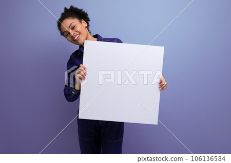 young pretty hispanic business woman with fluffy hair dressed in blue denim suit holding billboard 106136584