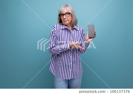 modern pensioner middle-aged woman with gray hair is studying smartphone gadget on bright studio 106137376