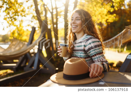 Fall concept woman drinking coffee on bench against backdrop of lake. Enjoying, solitude with nature 106137918