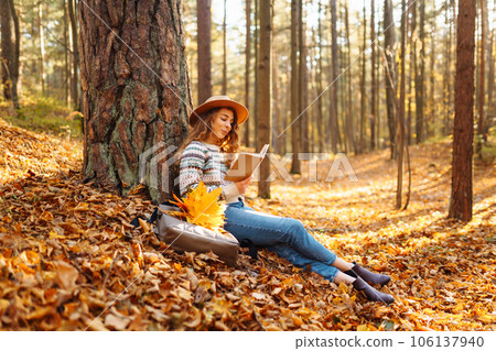 Stylish woman reading a book in the autumn park. Relaxation, enjoying, solitude with nature. Stylish woman reading a book in the autumn park. Relaxation, enjoying, solitude with nature. 106137940