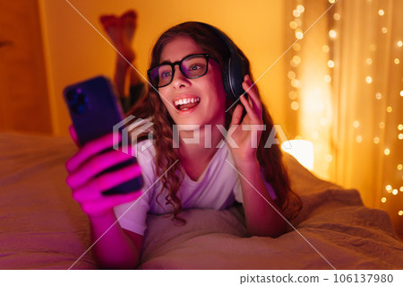 Woman in headphones before bedtime listening online to relaxing music. Remote work, internet concept Woman in headphones before bedtime listening online to relaxing music. Remote work, internet concept 106137980