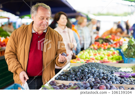 Elderly man buys plums at an open-air market Elderly man buys plums at an open-air market 106139104