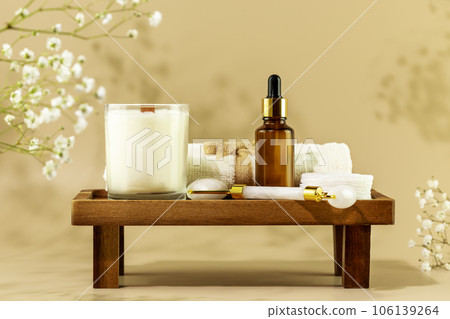 Eco friendly spa relax composition with serum, face roller, towel and candle on wooden podium on beige background with white flowers. Wellness and skin care treatment. Concept of me time and self care 106139264