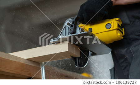 Master cuts the board with a circular saw in the workshop. Close-up of a carpenter's hands at work. Master cuts the board with a circular saw in the workshop. Close-up of a carpenter's hands at work. 106139727