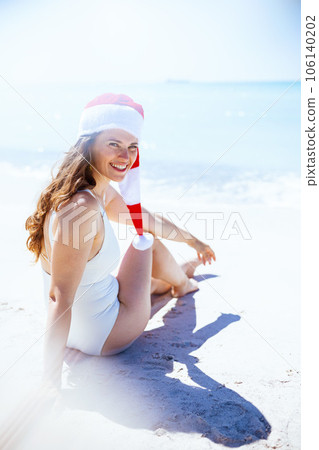 smiling modern female in white beachwear sitting at beach 106140202