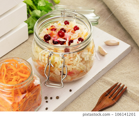 Probiotic food. Pickled or fermented vegetables. Korean carrot and sauerkraut in glass jars on a white board on a kitchen table. Home food preserving or canning. Close up 106141201
