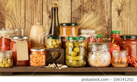 Autumn seasonal pickled or fermented vegetables, mushrooms in jars and bottle of cider placed in row on wooden background. Fall home food preserving or canning. Vegetarian and vegan foods, close up Autumn seasonal pickled or fermented vegetables, mushrooms in jars and bottle of cider placed in row on wooden background. Fall home food preserving or canning. Vegetarian and vegan foods, close up 106141202