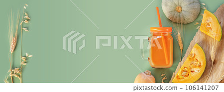 Eco friendly, autumn banner with glass of pumpkin juice with straw, pumpkins, rye and wheat ears on green background with copy space. The new crop of pumpkins. Autumn harvest of wheat, rye, pumpkins 106141207