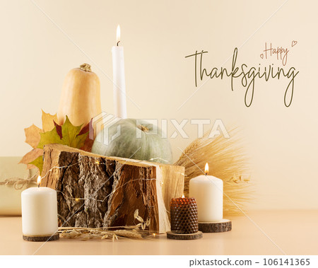 Thanksgiving congratulation card with pumpkins, dry autumn leaves, bouquet of rye and wheat ears, gifts and candles on a wooden podium on a beige background. Happy Thanksgiving Day Card 106141365
