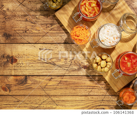 Probiotic food. Pickled or fermented vegetables. Lecho, sauerkraut, ajvar, korean carrot, olives in glass jars on a wooden background with shadows and copy space. Home food preserving or canning Probiotic food. Pickled or fermented vegetables. Lecho, sauerkraut, ajvar, korean carrot, olives in glass jars on a wooden background with shadows and copy space. Home food preserving or canning 106141368