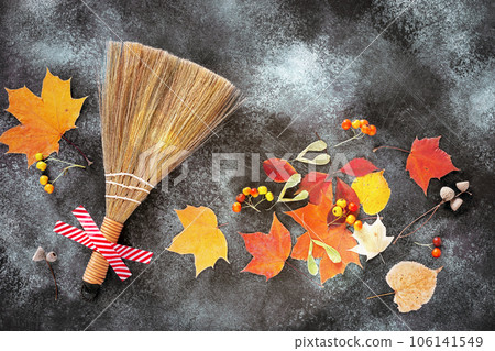 Autumn composition with a broom glued with tape, colorful autumn leaves, bunches of hawthorn and acorns on a dark gray asphalt background. The concept of the beauty of autumn under your feet 106141549