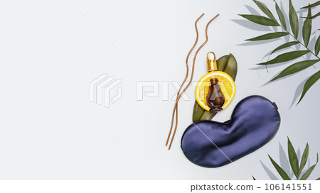 Relax composition with sleep mask, orange and orange oil in a bottle on a blue background with copy space. Orange oil is the best natural remedy for the treatment of depression, insomnia and stress 106141551