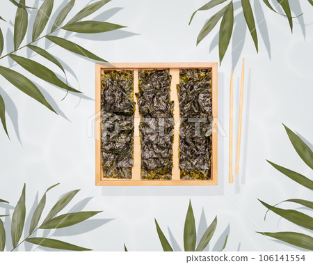 Healthy sea snack suitable for keto and vegan diet. Salty dried seaweed snack on a wood board, chopsticks and palm leaves on a blue background. Japanese food, chips of nori seaweed 106141554