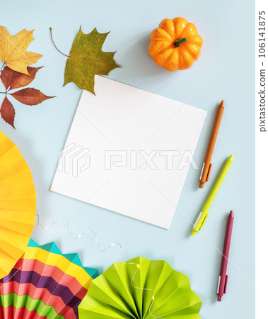 Autumn composition with white sheet of paper, colorful paper fans, pens and decorations on a blue background. A card for a children's art school. Autumn inspiration and creativity. Art workplace Autumn composition with white sheet of paper, colorful paper fans, pens and decorations on a blue background. A card for a children's art school. Autumn inspiration and creativity. Art workplace 106141875