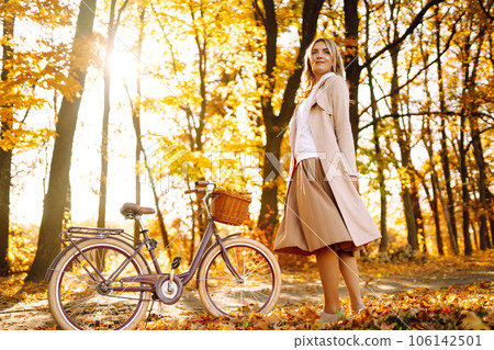 Stylish woman with a bicycle enjoying autumn weather in the park. Beautiful Woman in the autumn forest. 106142501