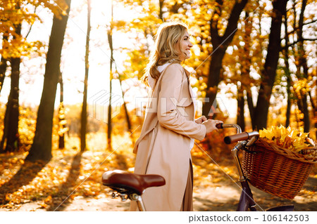 Stylish woman with a bicycle enjoying autumn weather in the park. Beautiful Woman in the autumn forest. 106142503