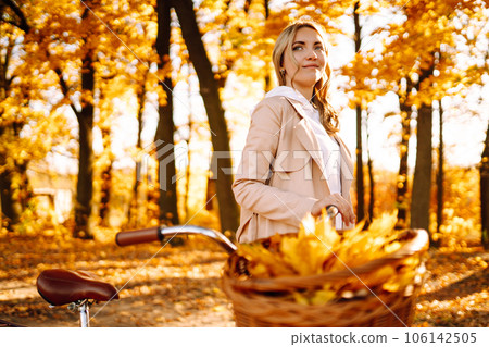 Stylish woman with a bicycle enjoying autumn weather in the park. Beautiful Woman in the autumn forest. 106142505