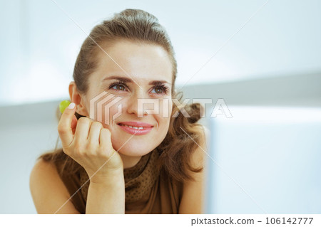 Dreaming young housewife eating grape in kitchen 106142777