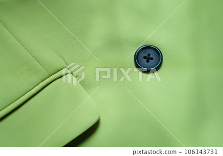 Black button is sewn on green cotton fabric closeup 106143731